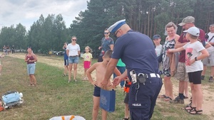 policjant pochylający się nad dzieckiem, które wyciąga z papierowej torby gadżet