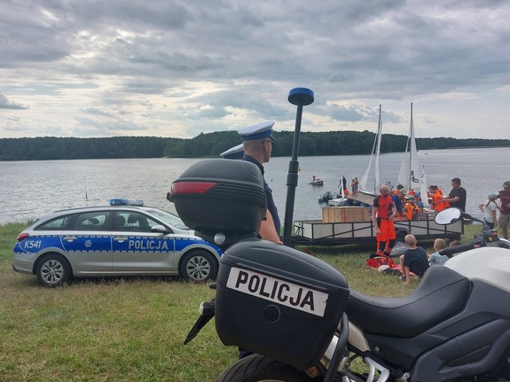 motocykl policyjny i radiowóz, w tle zalew i pływające żaglówki