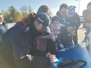 policjantka wykonująca odciski palców dziecku, obok stojący ludzie