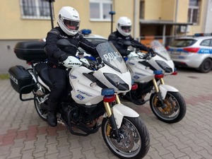 Policjanci w kombinezonach i kaskach siedzący na motocyklach