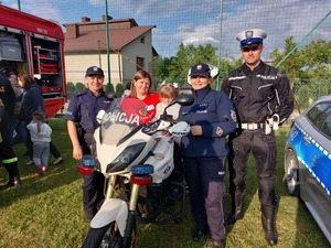 policjanci stojący obok motocykla, na którym siedzi dziewczynka, obok stoi kobieta