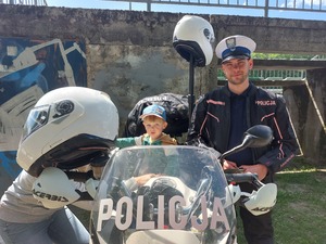 policjant stojący obok motocykla, na motocyklu siedzi dziecko