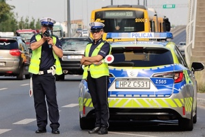 policjanci na tle radiowozu, jeden z policjantów trzyma miernik prędkości