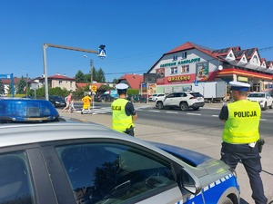 radiowóz i policjanci stojący przy drodze, w tle przejście dla pieszych