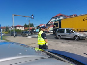 policjant stojący obok radiowozu, obok przejście dla pieszych