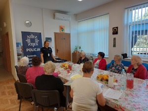 policjantki na spotkaniu z seniorami, na zdjęciu siedzący przy stole seniorzy oraz policjantki