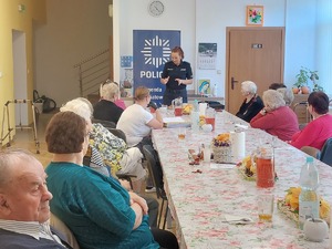 policjantki na spotkaniu z seniorami, na zdjęciu siedzący przy stole seniorzy oraz policjantki