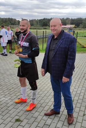 policjant w stroju sportowym ze statuetką dla najlepszego bramkarza, obok stoi mężczyzna