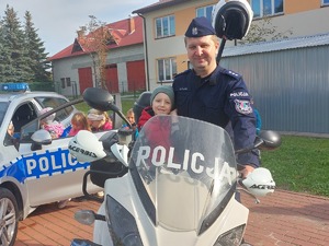 policjant stojący obok motocykla, na motocyklu siedzi dziecko