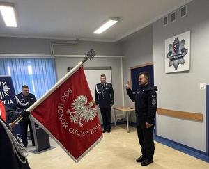 zdjęcie z uroczystości ślubowania. Na zdjęciu widoczny nowo przyjęty funkcjonariusz oraz poczet sztandarowy, w tle I zastępca Komendanta Powiatowego Policji w Kolbuszowej