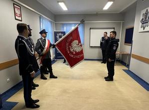 zdjęcie z uroczystości ślubowania. Na zdjęciu widoczny nowo przyjęty funkcjonariusz oraz poczet sztandarowy, w tle I zastępca Komendanta Powiatowego Policji w Kolbuszowej