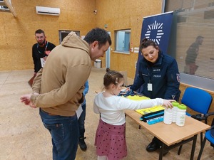 policjantka na stoisku profilaktycznym, przed stoiskiem dorośli i dzieci