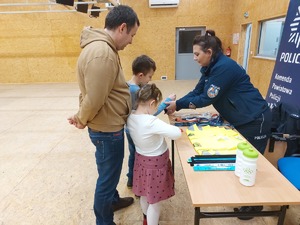 policjantka na stoisku profilaktycznym, przed stoiskiem dorośli i dzieci