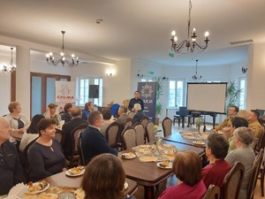 zdjęcia z debaty z seniorami. Na zdjęciu widoczne siedzące osoby oraz prelegenci - policjanci, kobieta w niebieskiej kamizelce z napisem SANEPID oraz strażacy.