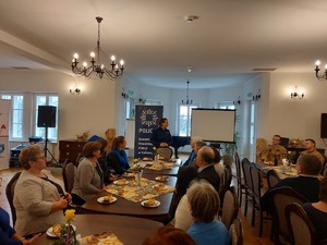 zdjęcia z debaty z seniorami. Na zdjęciu widoczne siedzące osoby oraz prelegenci - policjanci, kobieta w niebieskiej kamizelce z napisem SANEPID oraz strażacy.