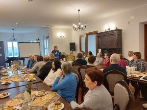 zdjęcia z debaty z seniorami. Na zdjęciu widoczne siedzące osoby oraz prelegenci - policjanci, kobieta w niebieskiej kamizelce z napisem SANEPID oraz strażacy.