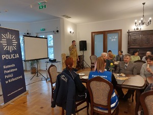 zdjęcia z debaty z seniorami. Na zdjęciu widoczne siedzące osoby oraz prelegenci - policjanci, kobieta w niebieskiej kamizelce z napisem SANEPID oraz strażacy.